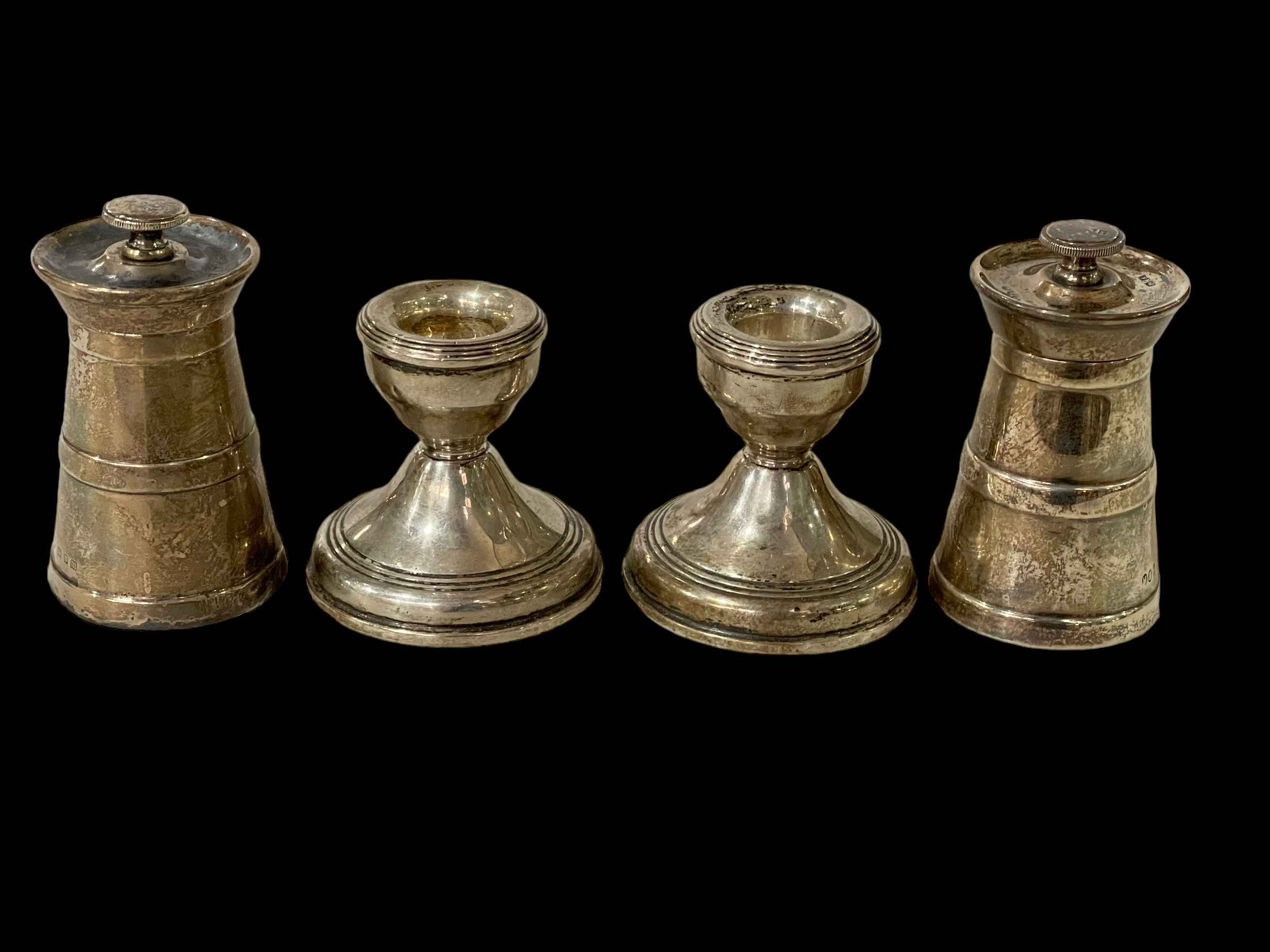 Two silver pepper grinders and pair silver dwarf candlesticks.