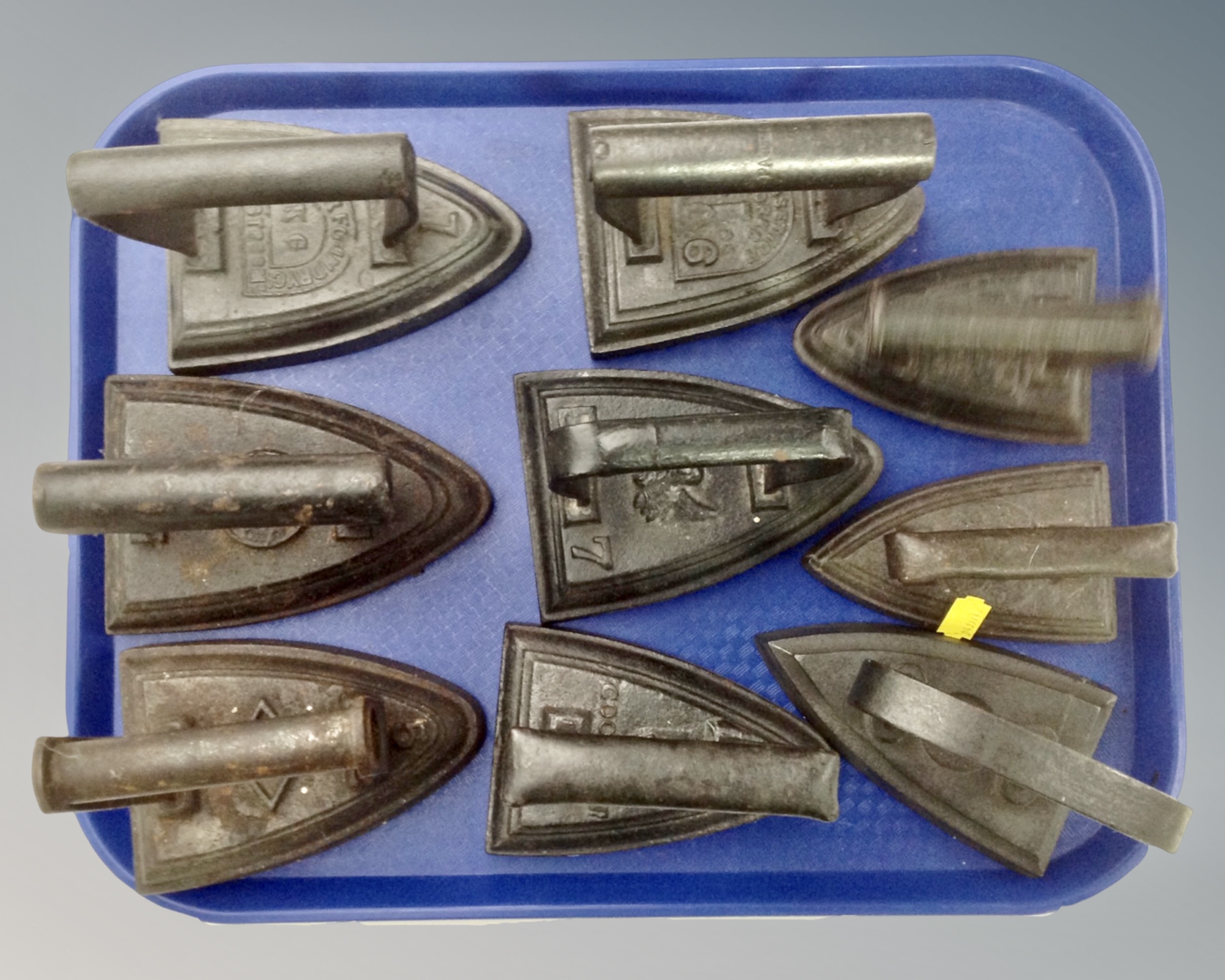 A tray containing eight antique flat irons.