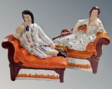 A pair of antique Staffordshire figures reclining on chaise longues.