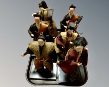 A tray containing six oriental dolls in traditional dress on stands.