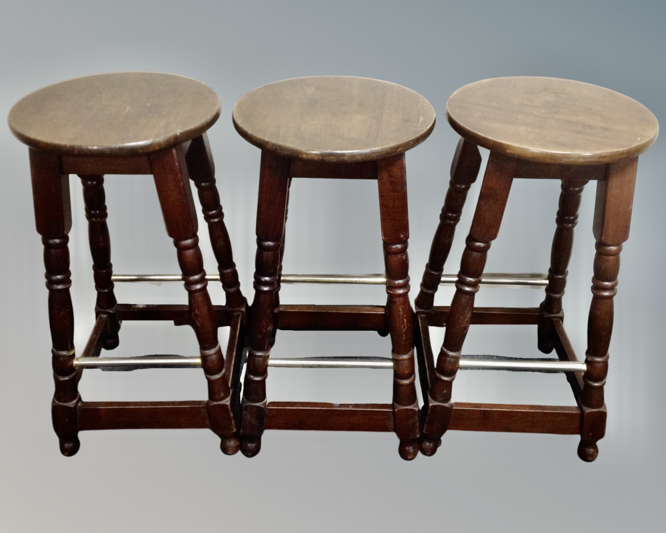 A set of three stained beech bar stools with foot rails.