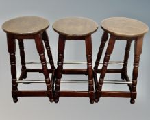 A set of three stained beech bar stools with foot rails.