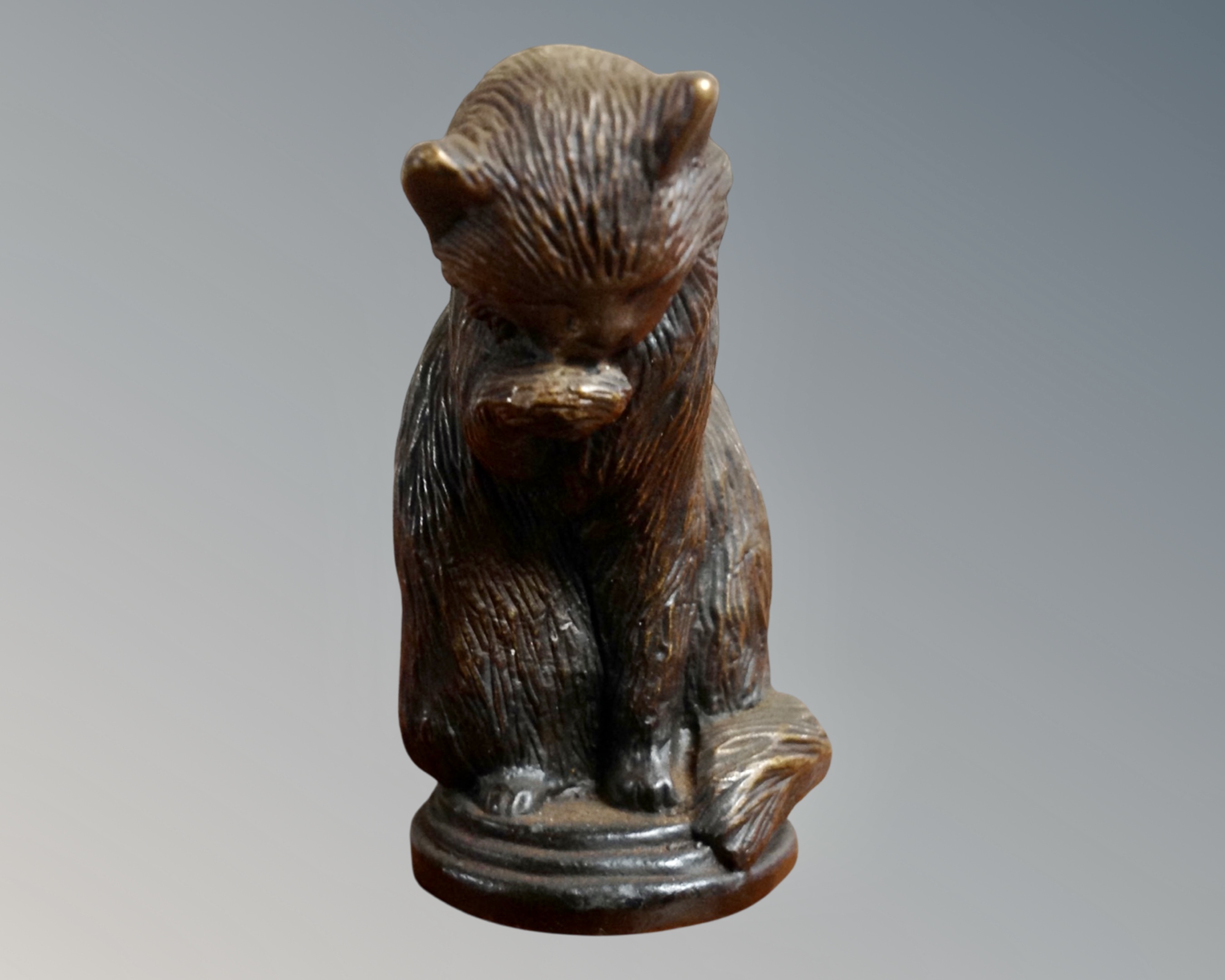 A bronze figure of a seated cat licking its paw,