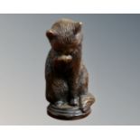 A bronze figure of a seated cat licking its paw,