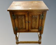 An Old Charm oak linen fold cabinet on raised legs.
