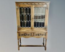 A carved oak double leaded glass door bookcase on raised legs,