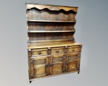 A carved oak triple door Welsh dresser fitted with cupboards and drawers beneath, retailed by W. E.
