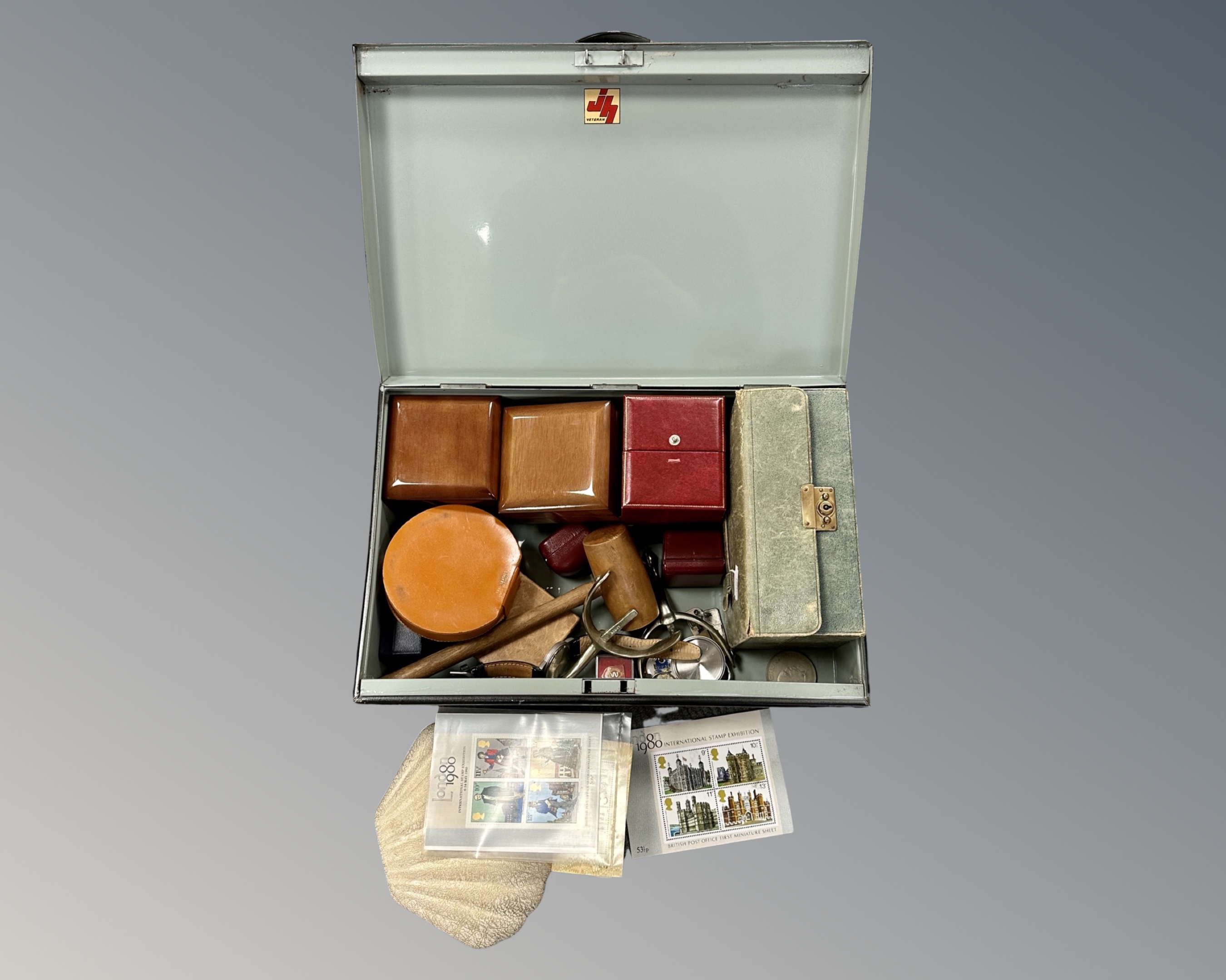 A metal deed box containing a gavel, a pair of spurs, a watch, a lapel badge, a padlock & keys,