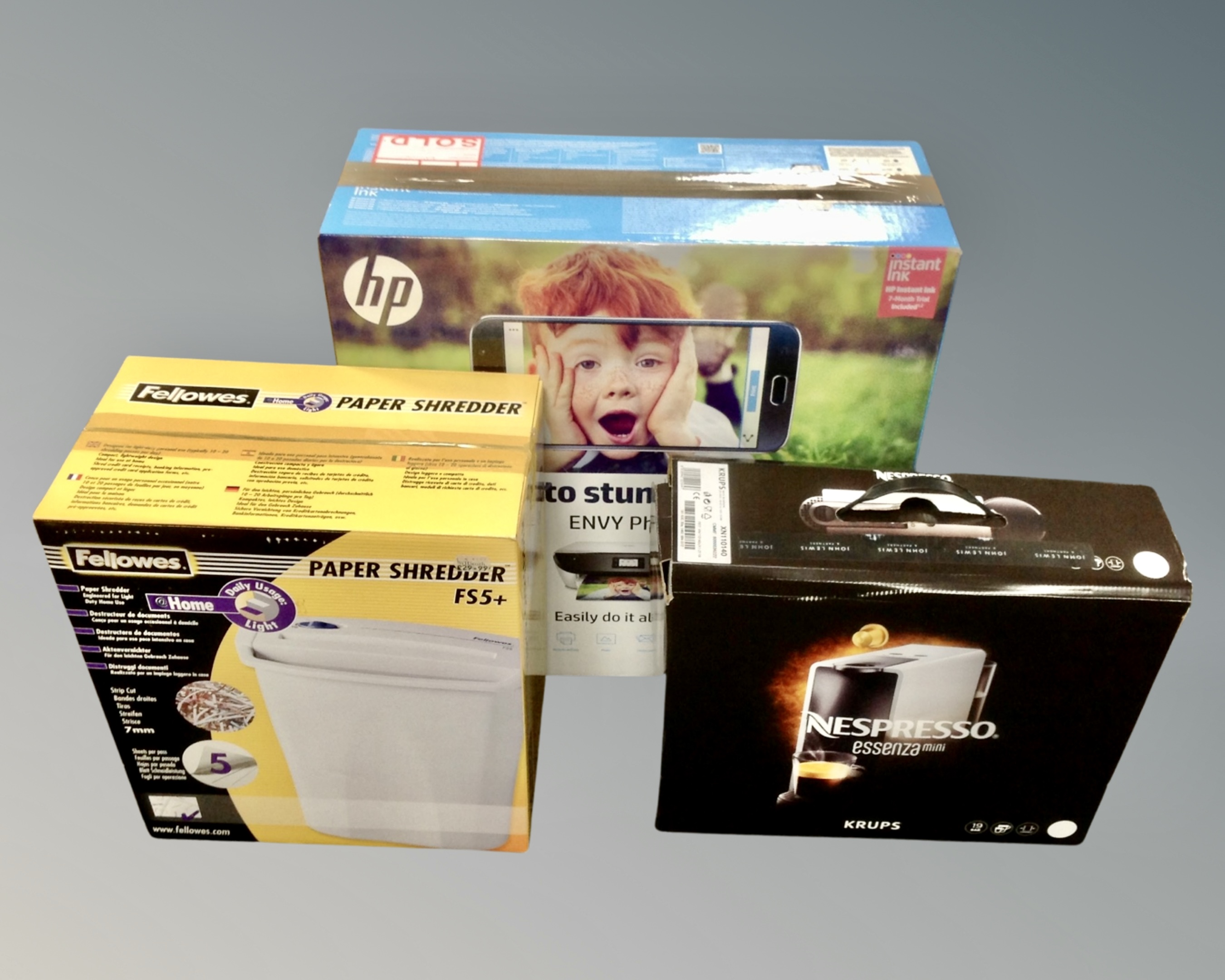 A boxed Nespresso Essenza mini coffee maker together with a boxed HP printer and a Fellowes paper