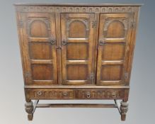 A Jacobean style carved three door sideboard fitted with two drawers beneath on raised legs (width