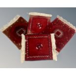 Four small fringed Afghan rugs on red ground.