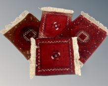 Four small fringed Afghan rugs on red ground.