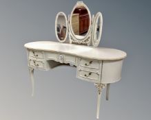 A cream and gilt kidney shaped dressing table on raised legs with triple mirror.