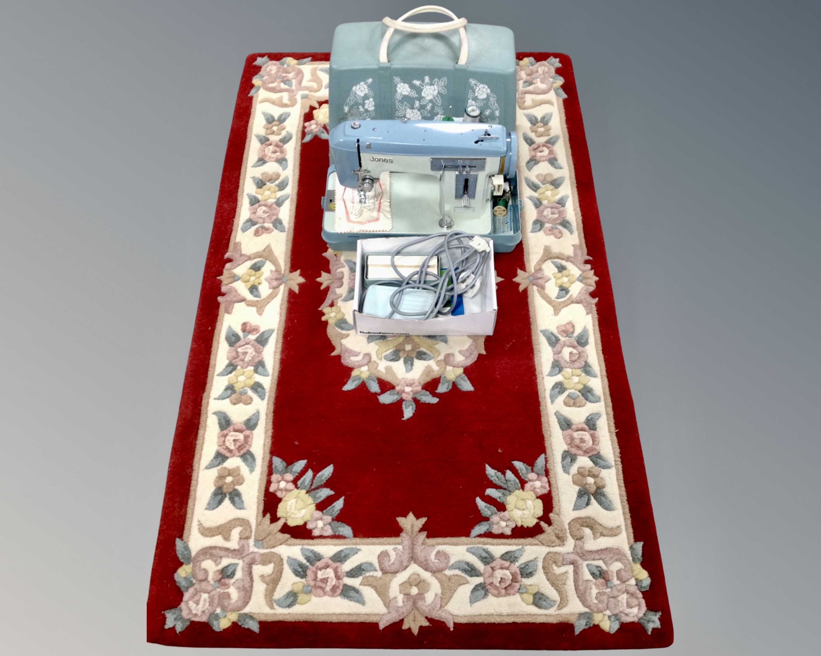 A Jones electric sewing machine with lead and pedal together with a Chinese rug on red ground.
