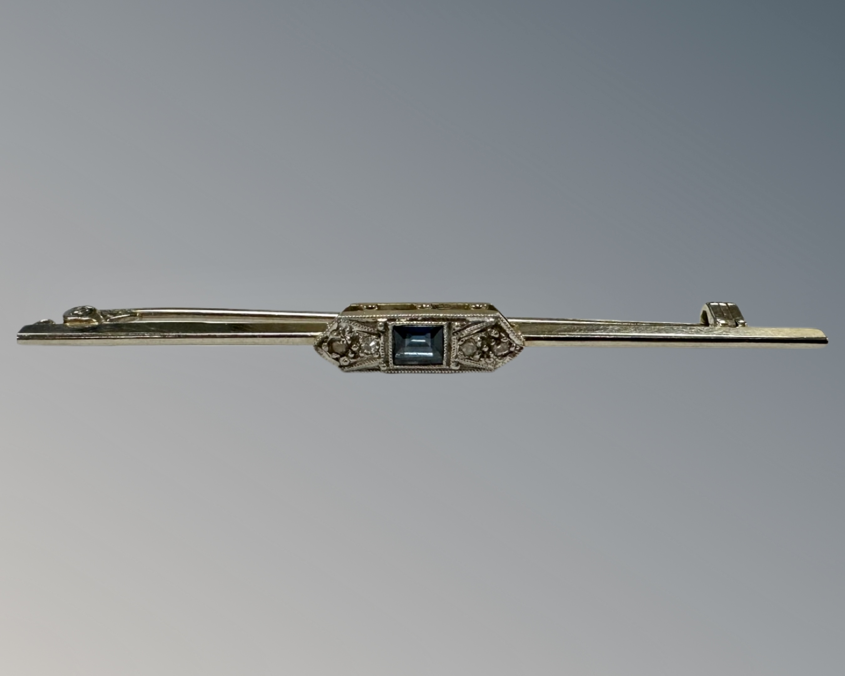 A 14ct white gold and platinum set diamond and sapphire bar brooch, width 65 mm, 3.7g.