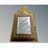 A brass cushion framed mirror containing two brass backed brushes.
