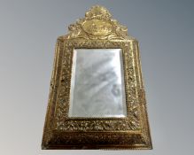 A brass cushion framed mirror containing two brass backed brushes.