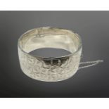 A engraved silver hinged bangle with safety chain, diameter 58mm.