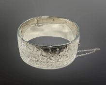 A engraved silver hinged bangle with safety chain, diameter 58mm.