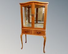 A yew wood double door arch topped display cabinet fitted with two drawers beneath, on raised legs.