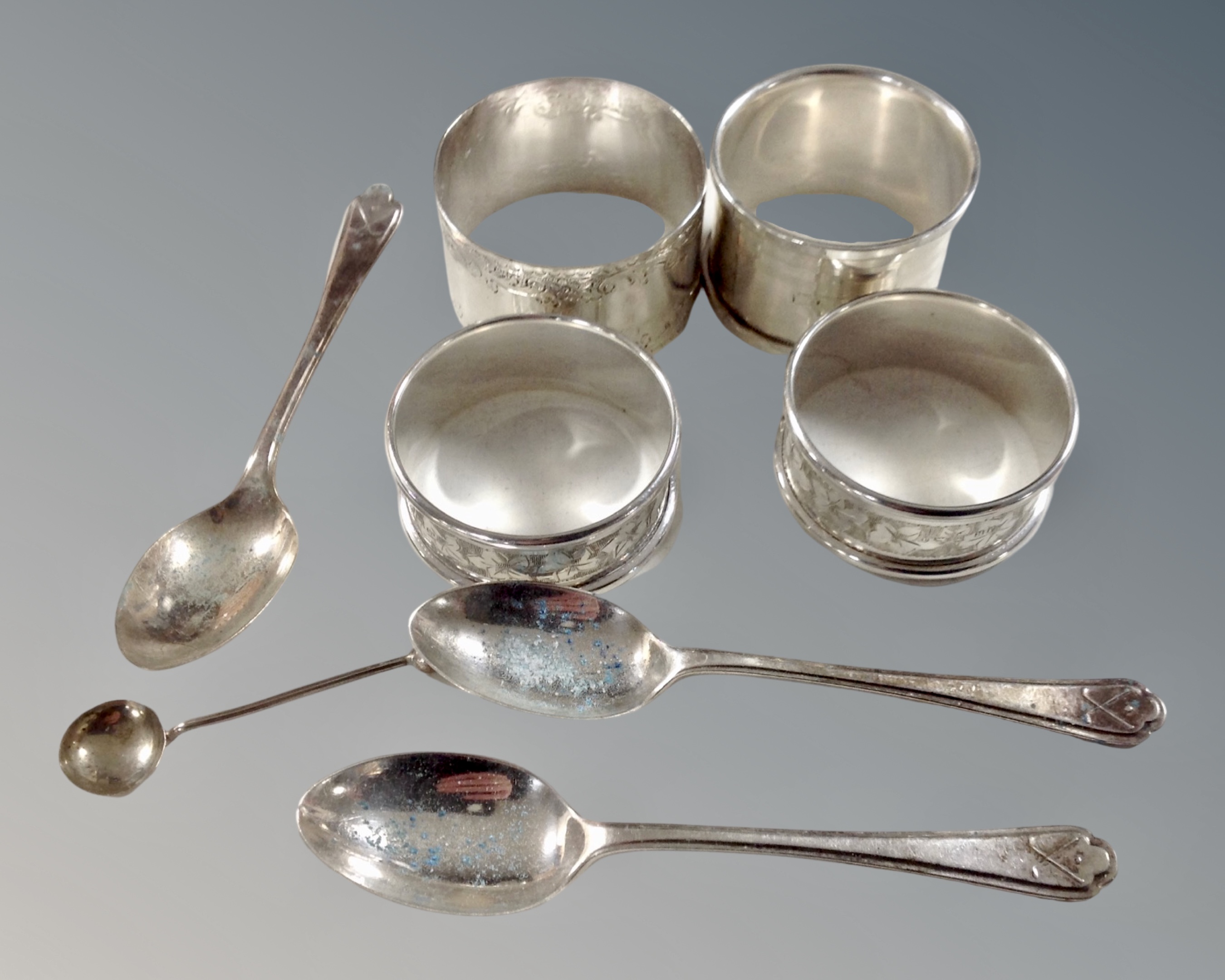Four silver napkin rings together with three silver teaspoons and a silver mustard spoon.
