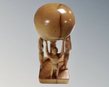 A wooden hand carving of four figures holding a globe aloft, signed H Stone, dated March 2007.