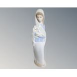 A Lladro figure of a woman in a shawl carrying flowers.