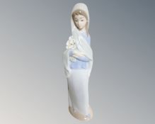 A Lladro figure of a woman in a shawl carrying flowers.