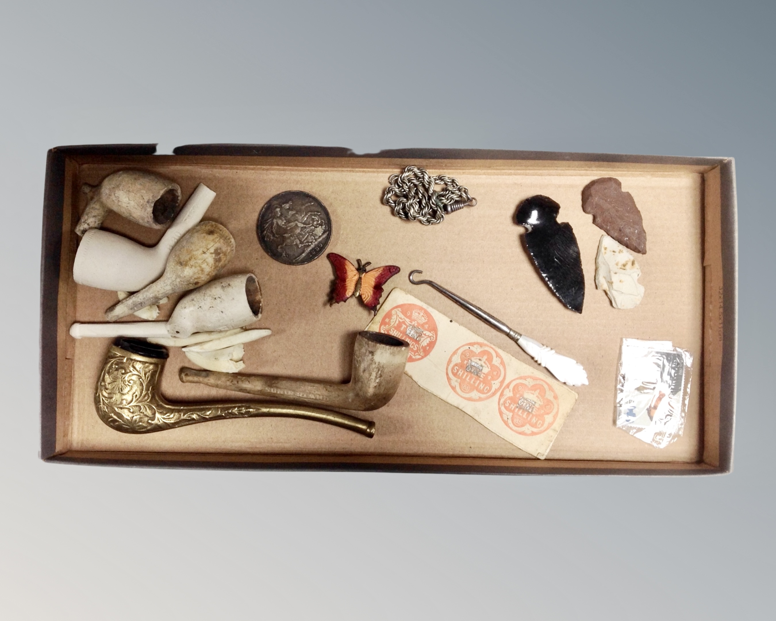 A tray containing an enamelled butterfly brooch, Victorian 1889 silver crown, pipes, arrowheads,