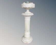 A classical style column and fruit bowl containing polished stone eggs,