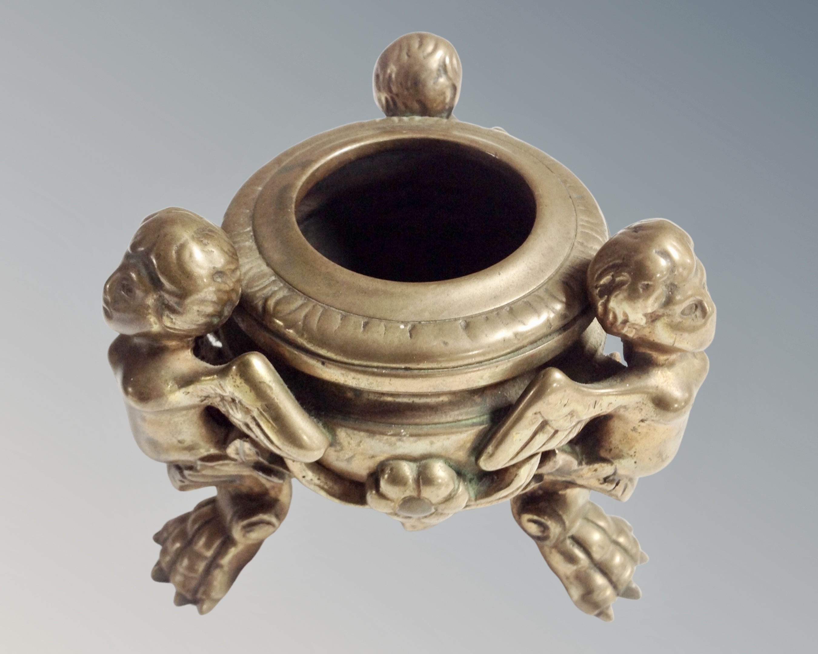 A circular brass bowl supported by three winged cherubs, height 9.