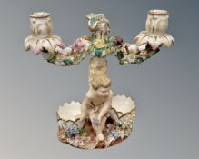 A pair of continental porcelain twin branch candelabrum decorated with putti (a/f)