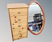 A narrow pine five drawer chest together with an oval pine framed mirror.