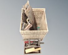 A wicker lidded basket containing vintage hand saws together with further wooden caddy containing