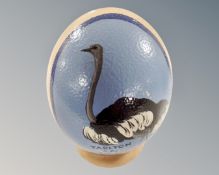 A hand-painted ostrich egg on wood stand.