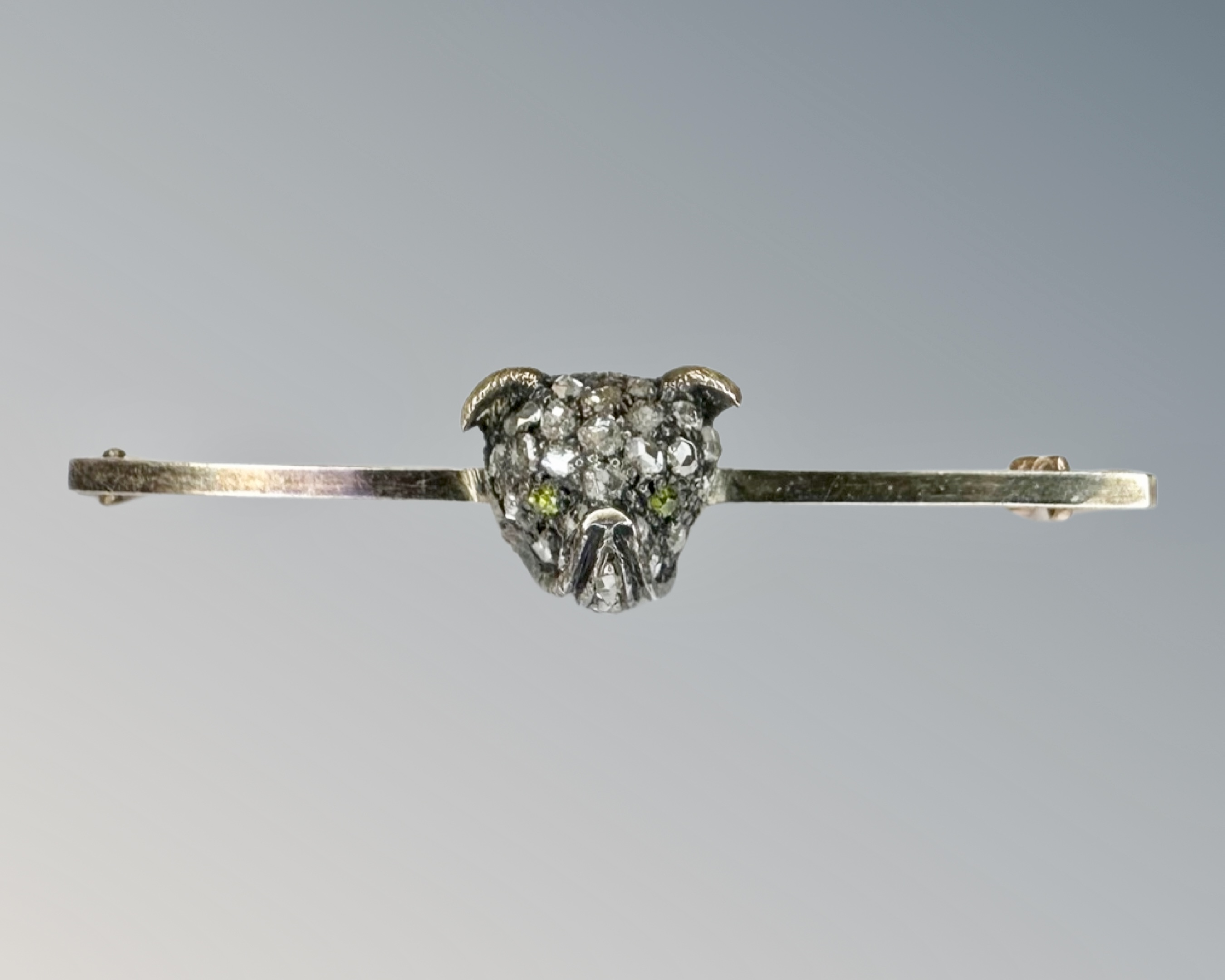 An antique bar brooch modelled as a diamond encrusted pug's head, set with peridot eyes,