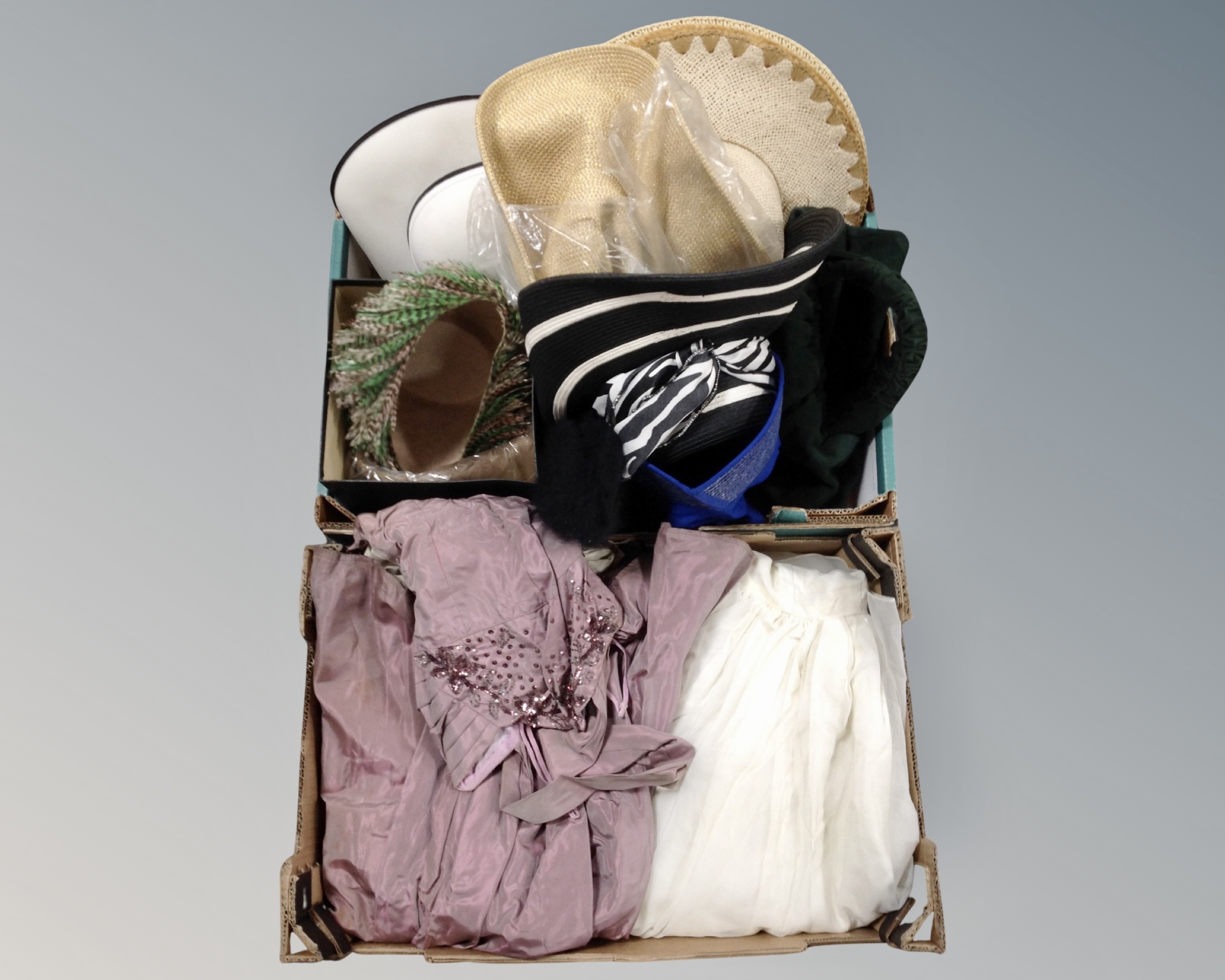 Two boxes containing two lady's dresses and a quantity of hats including straw and feather examples.