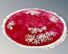 A circular fringed Chinese rug on maroon ground.