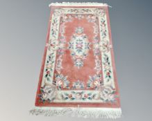 A Chinese floral embossed fringed rug on pink ground.