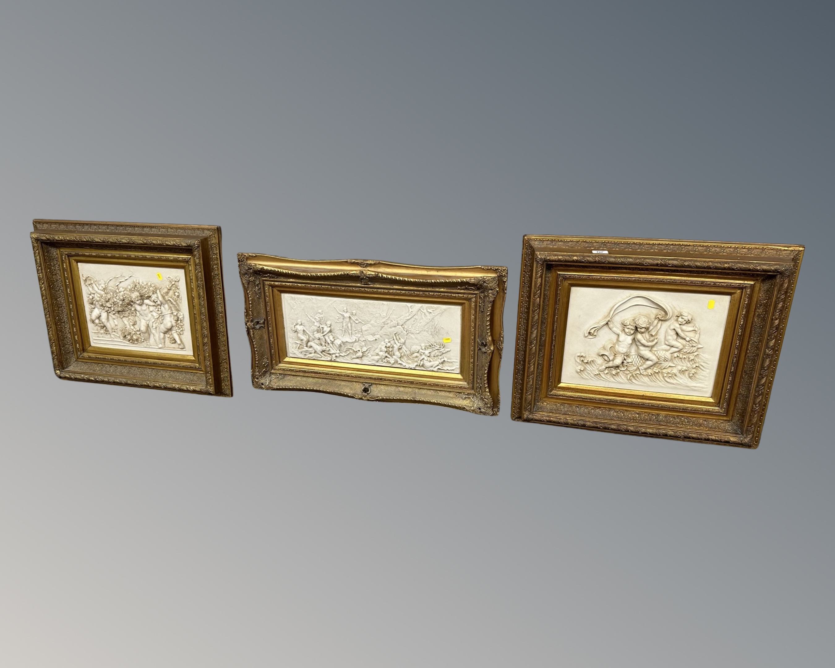 Three gilt framed relief plaques depicting cherubs, largest measures 83cm wide.