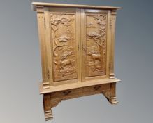 A heavily carved oak double door cabinet with two drawers beneath on raised legs