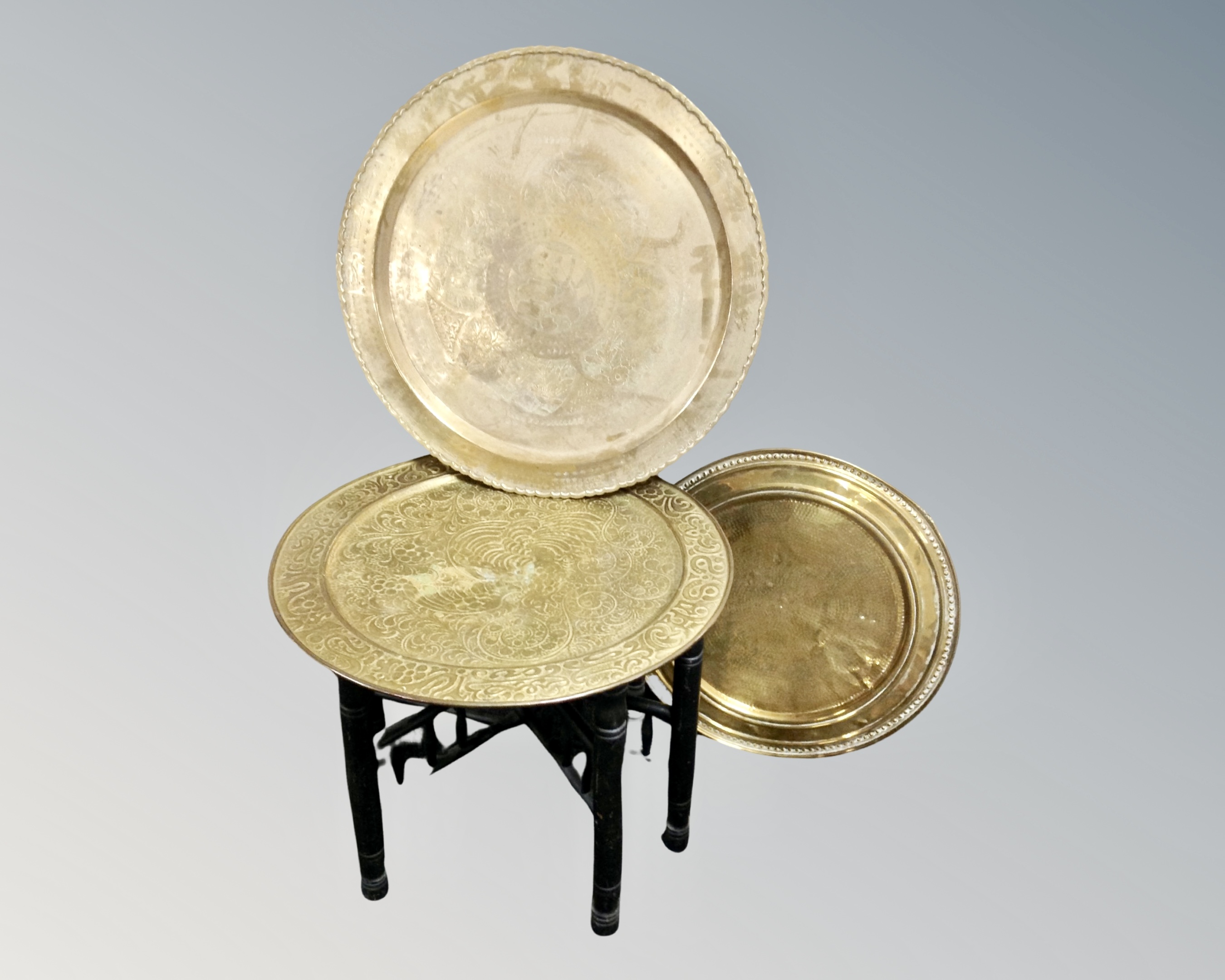 A folding brass topped Eastern occasional table together with two further brass trays.