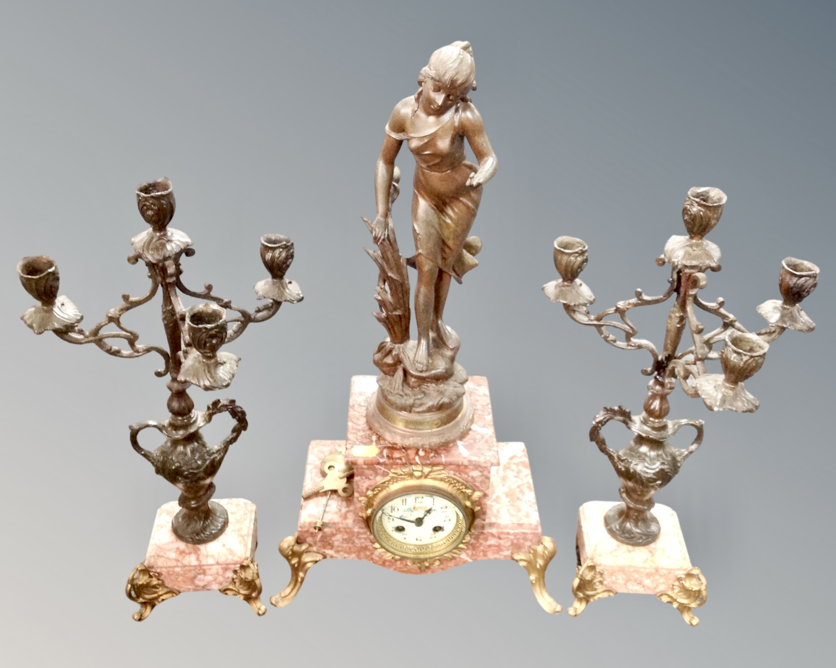 A three piece patinated metal and rouge marble clock garniture set, with pendulum and key.