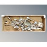 A wooden tray containing antique and later cutlery, sugar tongs, fruit spoons, etc.