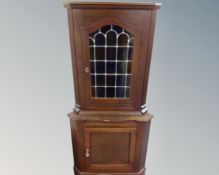 A stained oak corner cabinet with leaded glass door,