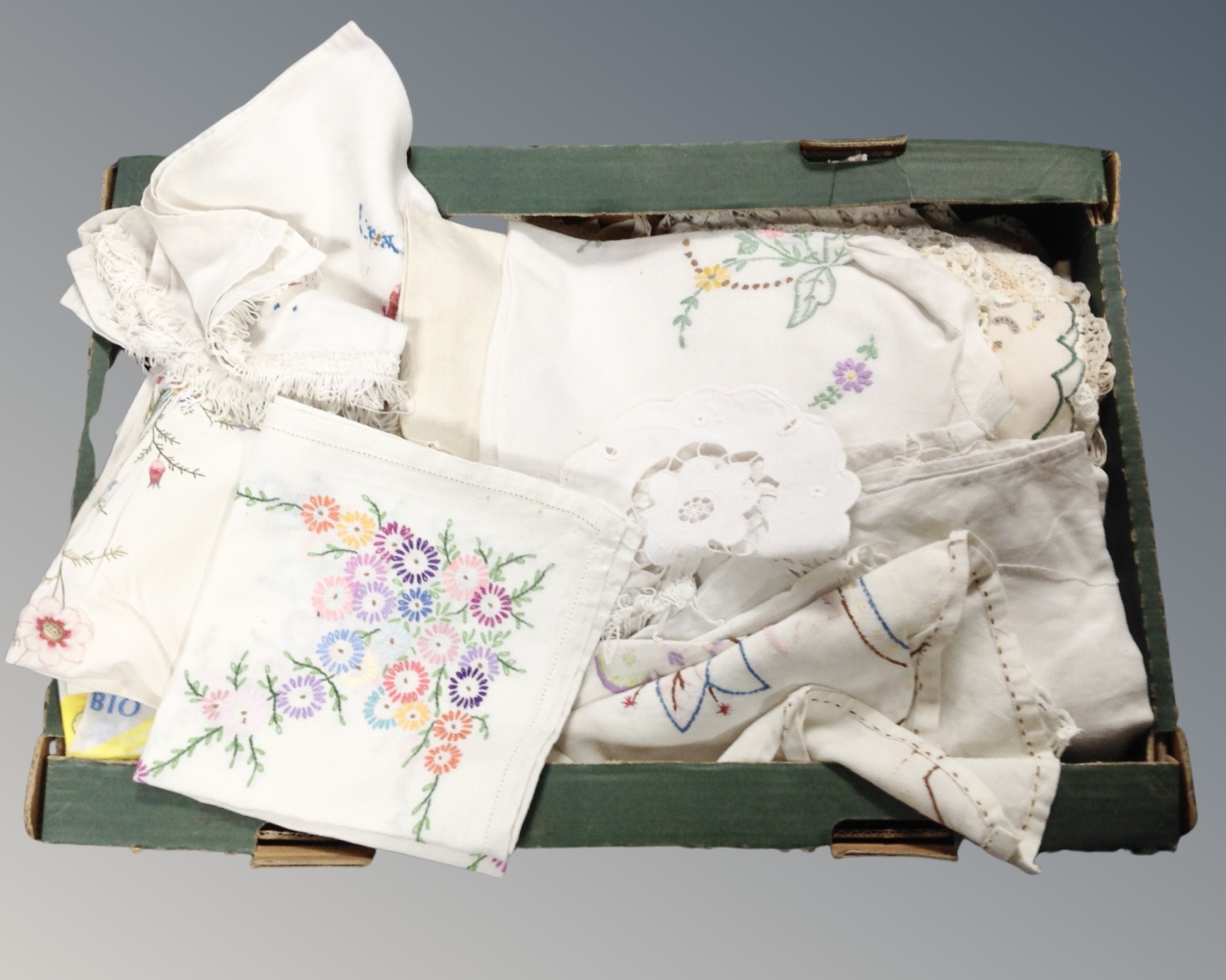 A box containing a quantity of assorted table linens including needlework examples.