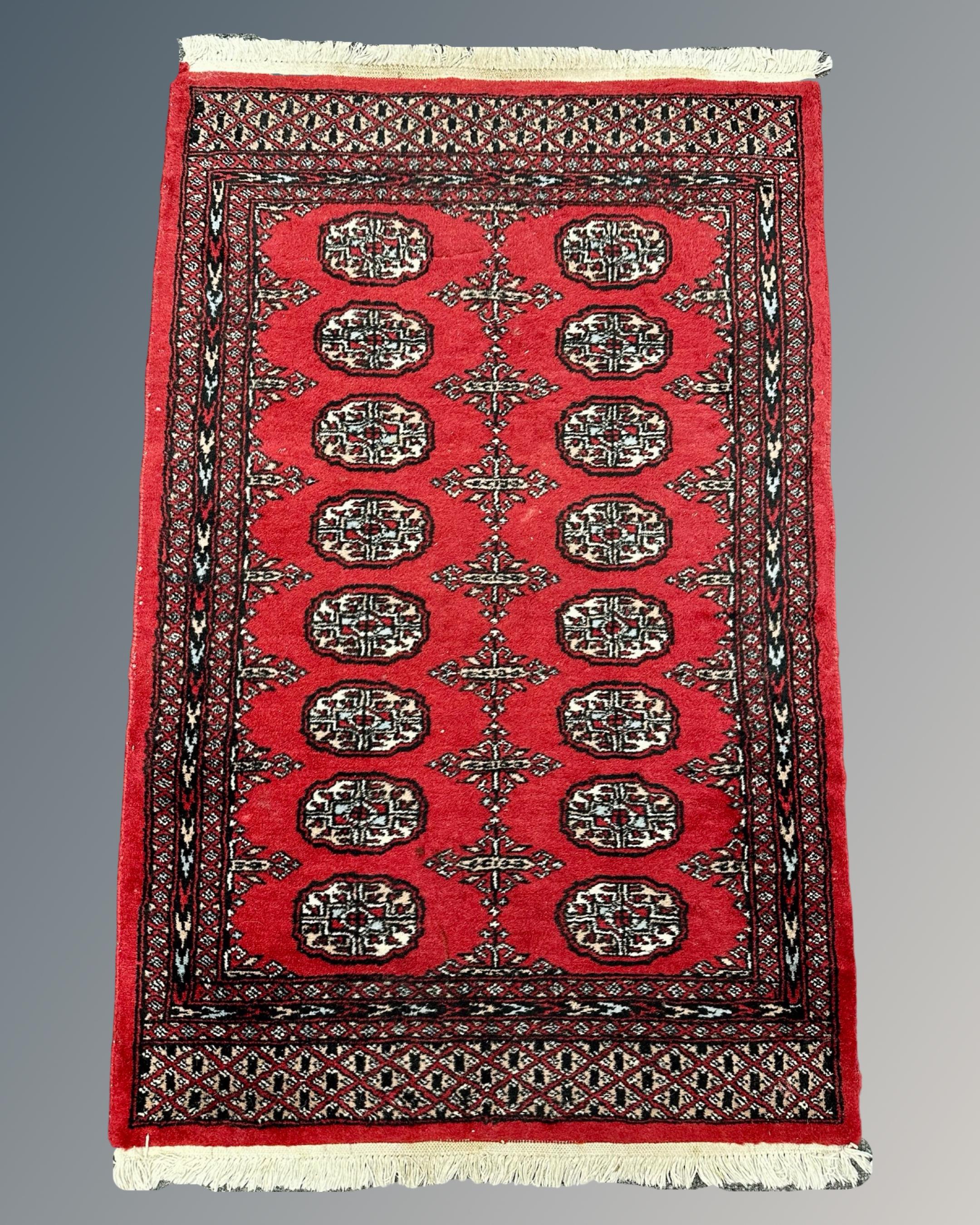 A Bokhara design rug on red ground, 76cm by 120cm.
