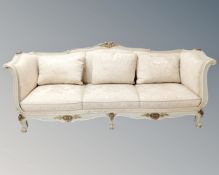 A cream and gilt baroque style three seater settee.
