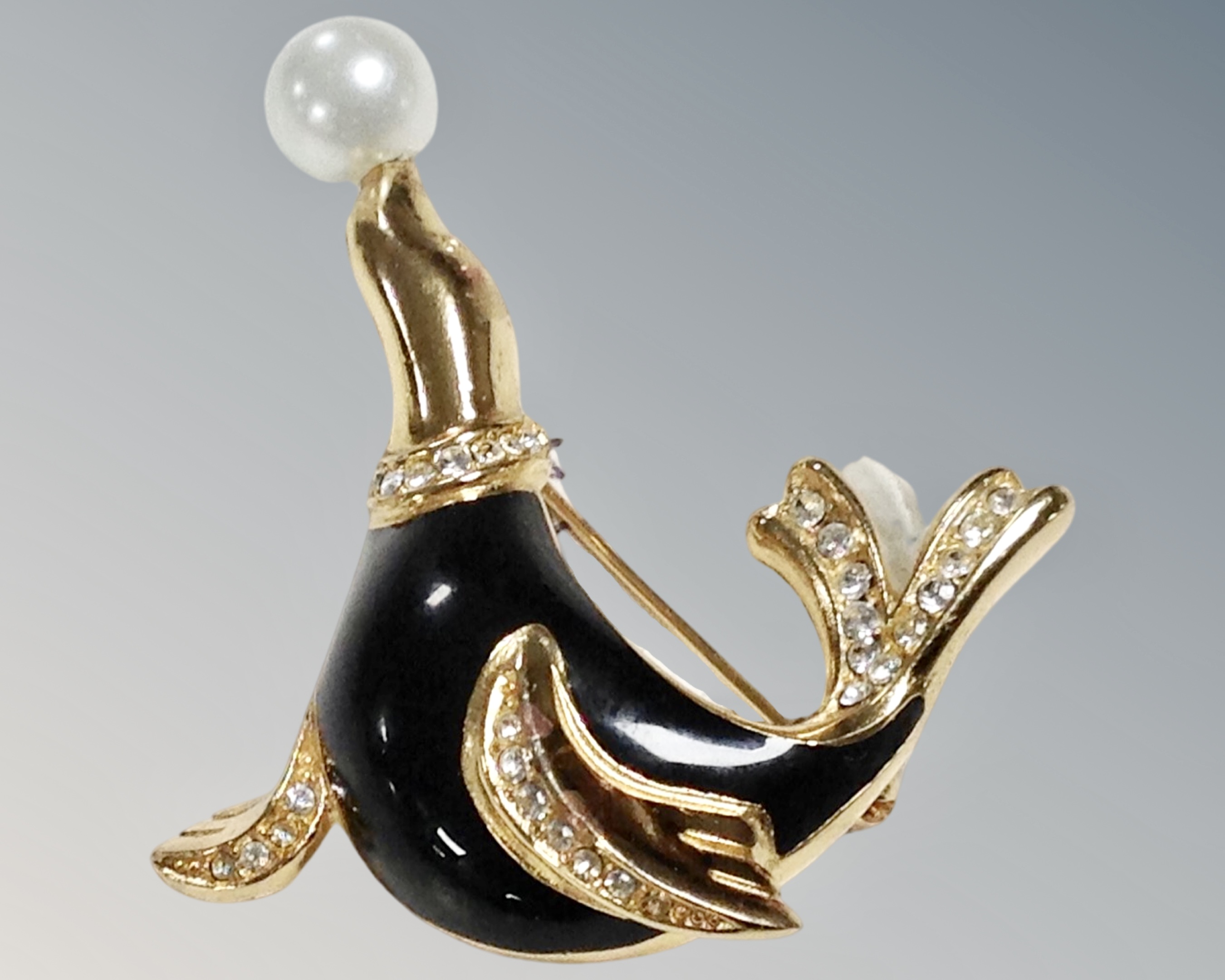 A Christian Dior yellow metal, enamel and white stone set seal brooch balancing a pearl on nose.