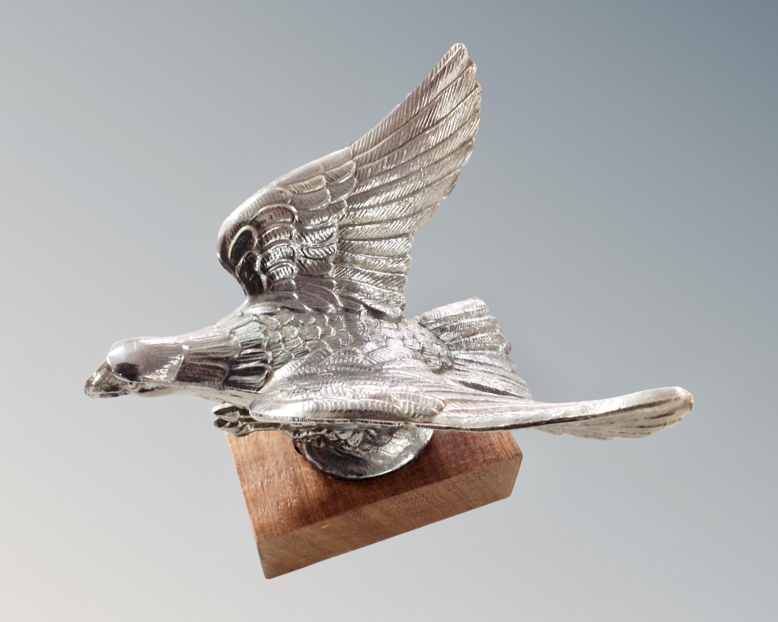 An eagle car mascot, mounted on a wooden plinth.